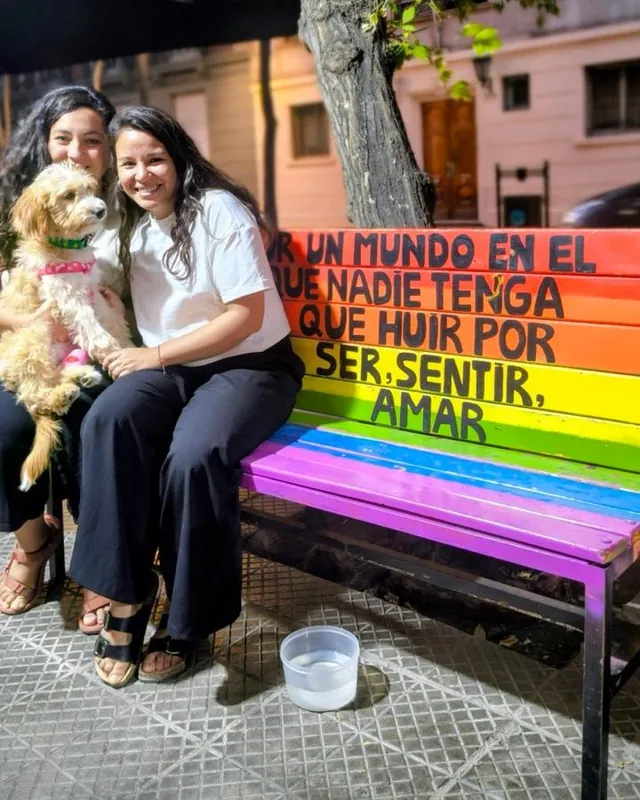 Dos personas con su perro en la banca arcoíris de la terraza, de noche