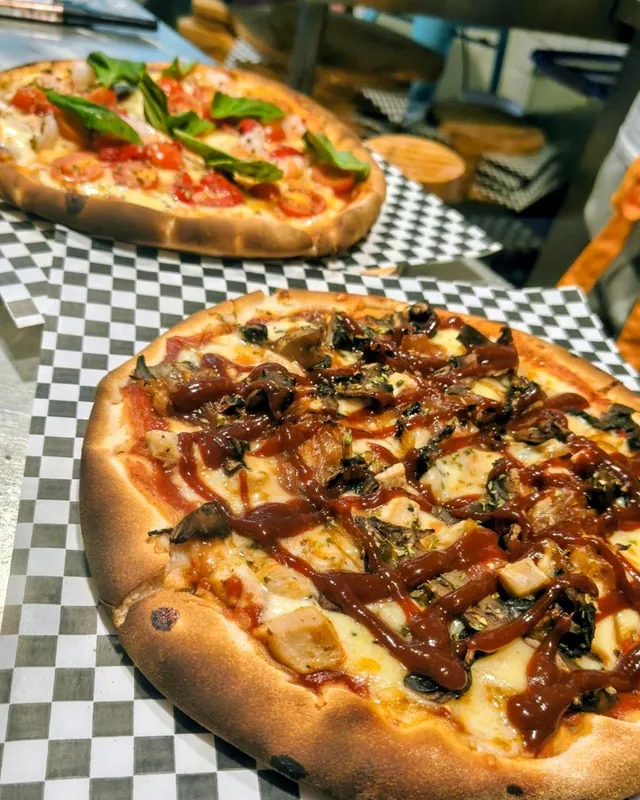 Dos pizzas recién horneadas en la cocina, una con salsa BBQ