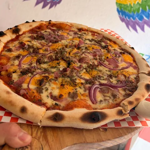 Pizza Lela con carne, cebolla morada, tocino y queso cheddar, frente al muro de alas arcoíris