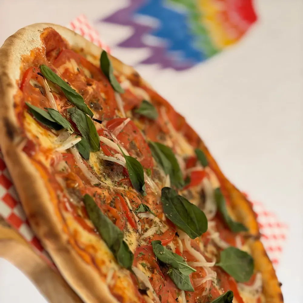 Pizza Chilenita recién horneada, con el arcoíris pintado del local de fondo